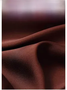 Dettaglio macro del tessuto in raso marrone scuro con pieghe morbide e texture lucida