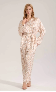 Full body view of women's satin pajama set with orange abstract print and waist belt