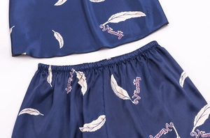 Detail showing smooth satin fabric texture with white feather prints on dark blue pajamas