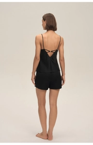 Détail d'un pyjama en satin noir montrant des brides croisées et des boucles en métal doré