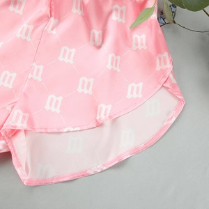 Close-up of pink satin pajama shorts featuring white letter M print and neat rolled hem
