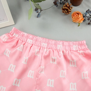 Detail view of pink satin pajama shorts with elastic waistband and floral letter print