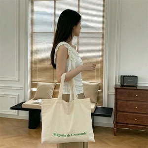 Detalle del bolso tote de lona grande con estampado de croissants verde y correa