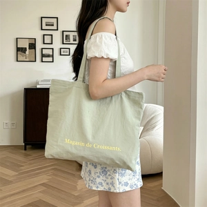 Detalle del bolso tote de lona verde claro con estampado llevado al hombro por la modelo