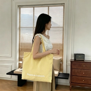 Vista lateral de un gran bolso tote de lona amarillo con texto llevado por una modelo