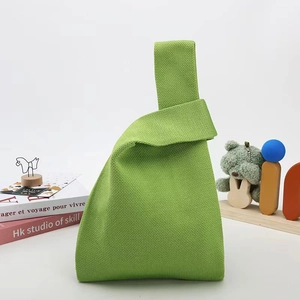 Detail view of avocado green knit handbag with cross-handle closure on a wooden desk