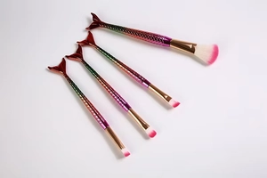 Macro view of four-piece gradient mermaid makeup brushes with fishtail scale texture
