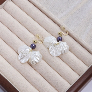 Detail of petal shell earrings with deep purple pearls and golden clip-on backings