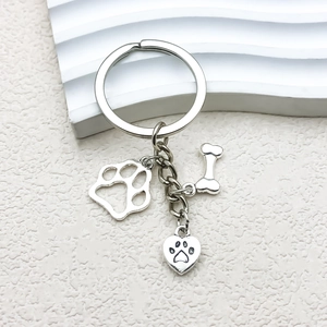 Macro view of silver metal dog bone and paw charms on a minimalist heart keychain