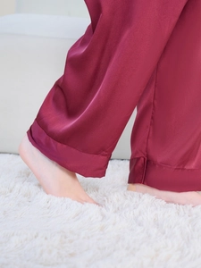 Close-up of wine red silk pajama pants with cuffed hems on a plush white carpet
