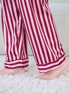 Detail of red and pink striped satin pajama pants hem on a plush white rug