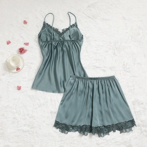 Pyjama en soie vert sauge avec dentelle noire posé sur un tapis en peluche blanc