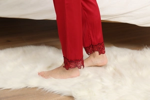 Detail of red satin pajama pants with black lace floral embroidery hem on white rug