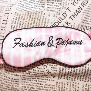 Pink striped satin sleep eye mask with Fashion & Pajama embroidery on newspaper background
