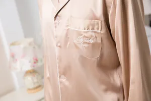 Detailed view of champagne satin pajama top with white piping and embroidered chest pocket