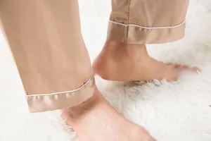 Close-up of champagne satin pajama pants with white silk piping on white rug