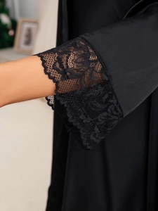 Detail of eyelash lace trim on black satin sleeves of a luxury silk nightgown