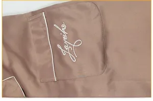Macro detail of men's satin pajama pocket featuring white contrast piping and embroidery