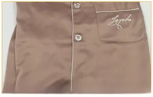 Detail of champagne satin pajama pocket with white piping and logo embroidery