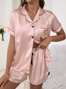 Détail d'un pyjama en satin rose clair avec liseré noir et motif cœur sur la poche