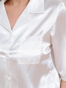 Detail of white satin ice silk pajamas featuring lace trim pocket and glossy texture