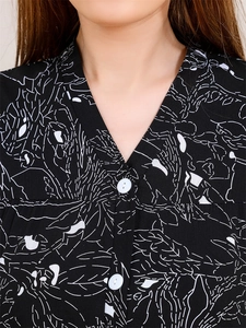 Détail du col en V d'un haut de pyjama noir à motifs floraux et petits boutons blancs