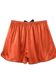 Detail of orange ice silk sleep shorts featuring a black bow and contrast piping finish