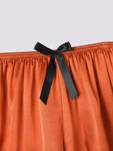 Detail of orange ice silk pajama shorts featuring elastic waist and black satin bow accent