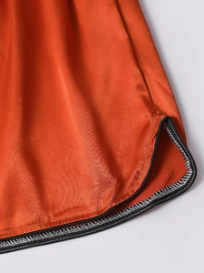 Detailed close-up of orange silk sleep shorts featuring contrast stitching and side slits