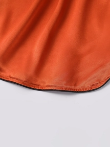 Detailed close-up of orange satin fabric with black piping trim and smooth silk texture