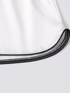Close-up of white ice silk shorts with curved hem and black contrast piping detail