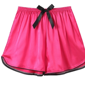Detail view of rose pink satin lounge shorts with black bow tie and curved hem design