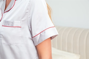 Détail d'un haut de pyjama en satin de soie argenté avec liseré rouge et poche
