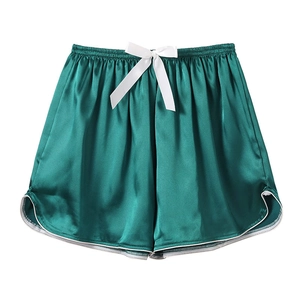 Detailed view of dark green satin sleep shorts with white bow and curved hem