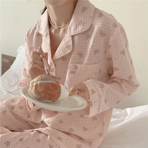 Pyjama rose à carreaux avec motifs d'ours et col à revers présenté sur un lit blanc