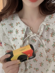 Close-up of minimalist gold necklace with irregular pendant worn with a floral cotton shirt
