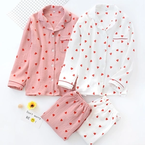 Flat lay of pink and white cotton pajamas with red heart prints and piping details