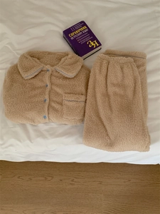 Detail view of beige fleece pajama set with blue piping and buttons on white bedsheets