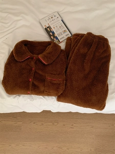 Detail view of brown fleece pajamas with pink trim and button-up front on white bedding
