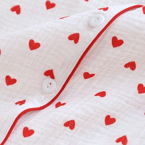 Detail shot of white cotton gauze pajama fabric with red heart print and button closure