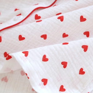 Close-up of white cotton gauze pajama fabric with red heart print and detailed red piping