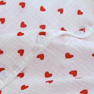 Macro shot of white crepe cotton fabric with red hearts and button details on pajamas
