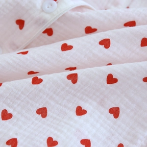 Detail of soft white cotton crepe fabric featuring red heart patterns and round button