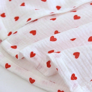 Detailed close-up of breathable white double gauze cotton fabric with red heart pattern