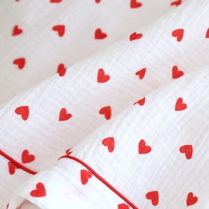 Detail of white cotton gauze pajama fabric with red heart patterns and piping