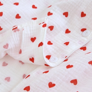 Close-up of soft white cotton crepe pajama fabric with red heart prints and buttons