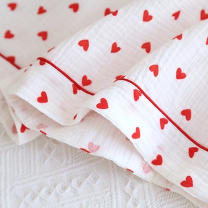 Detail of soft cotton gauze fabric with red heart prints and delicate piped edges
