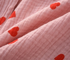 Close-up of pink cotton gauze fabric with red heart pattern and soft breathable texture
