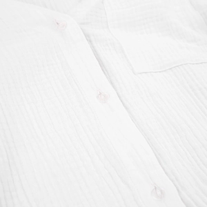 Close-up of white cotton double gauze fabric texture with resin buttons and pocket stitching