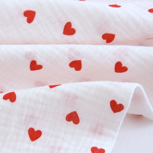 Detailed macro view of white cotton crepe fabric with red heart prints and soft texture